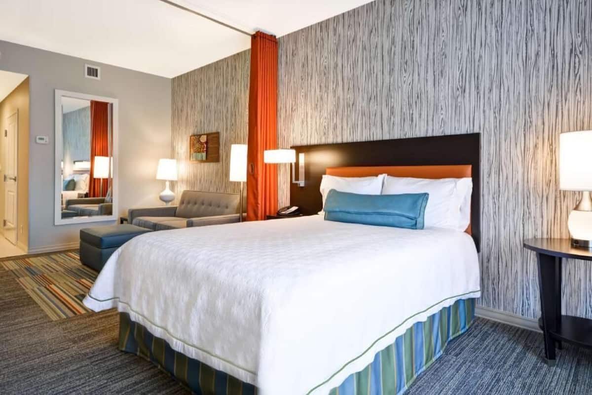 A hotel room with a large bed, a chair, a desk, and a mirror.
