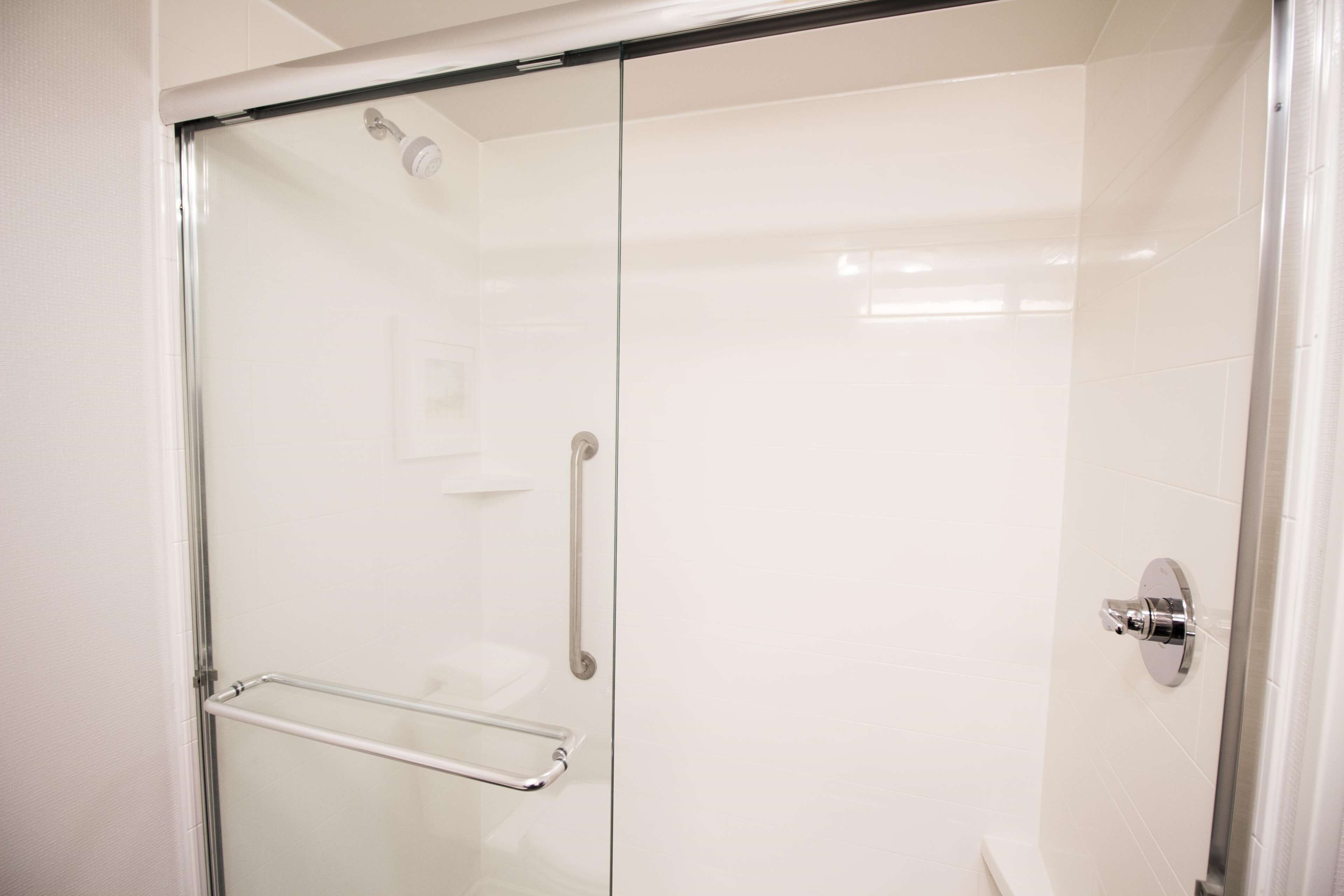 A glass-enclosed shower with a handrail, a wall-mounted faucet, and a control panel.