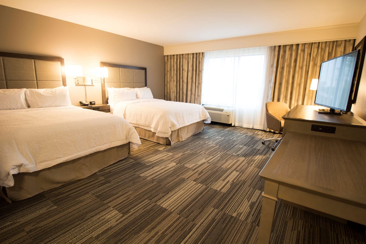 Een hotelkamer met twee bedden, een bureau, een televisie en een groot raam met gordijnen.