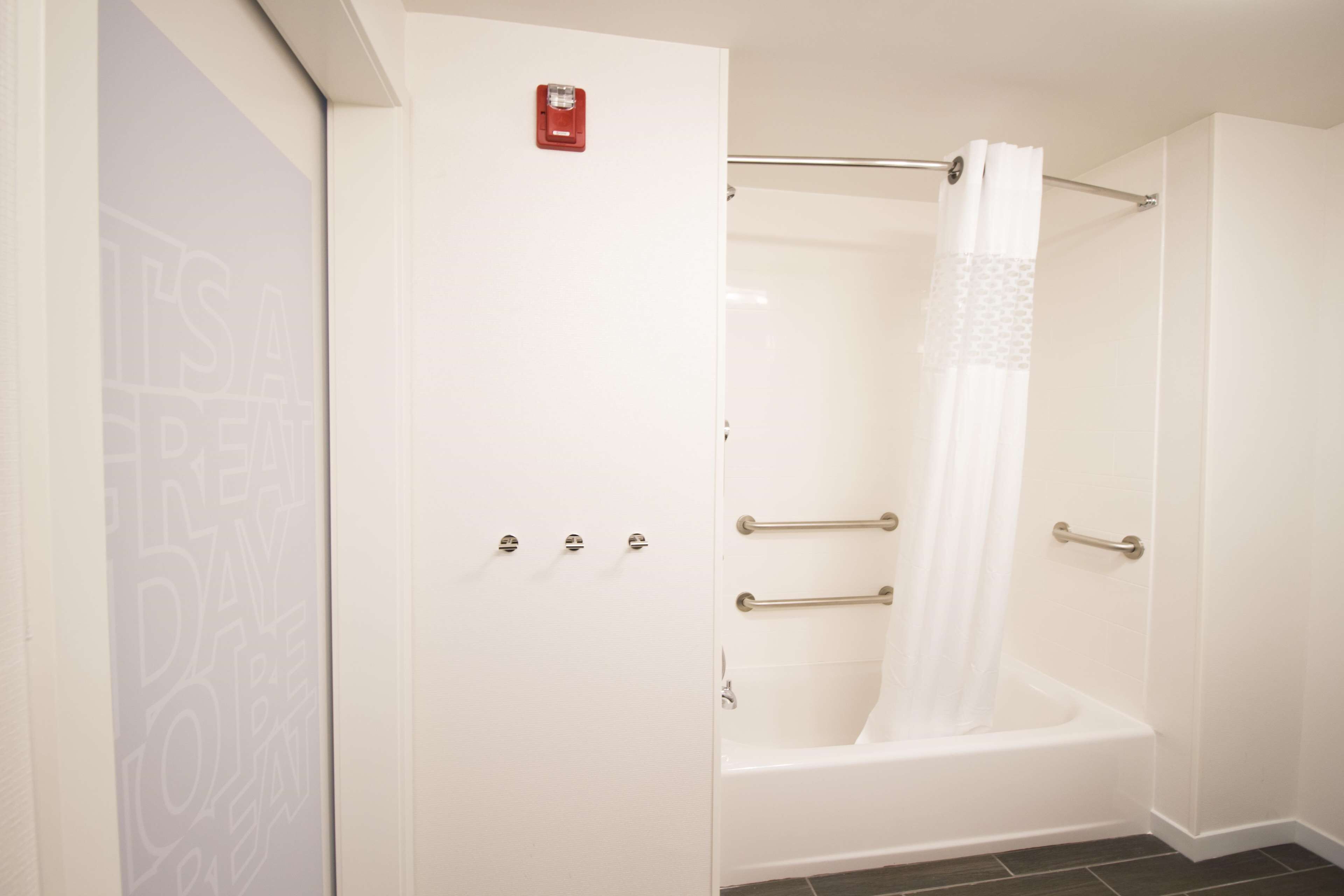 Un baño con una bañera blanca, una cortina de ducha y una puerta con detector de incendios.