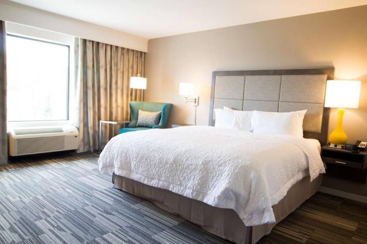Een hotelkamer met een groot bed, een stoel, een bureau en een raam met gordijnen.