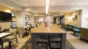A hotel lobby with a long bar, seating area, and a television mounted on the wall.