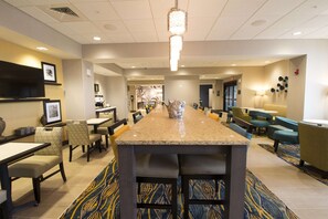 A hotel lobby with a long bar, seating area, and a television mounted on the wall.