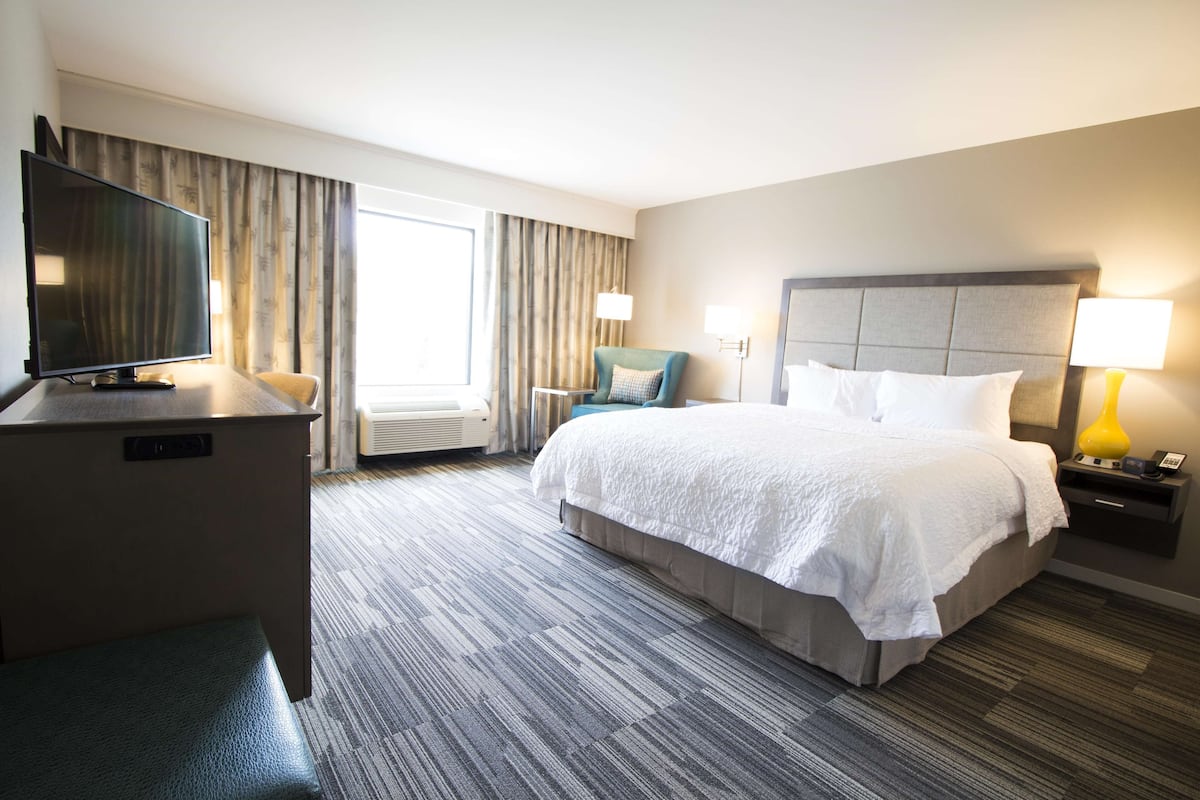 Hotelkamer met een bed, televisie, bureau, stoel, lamp en raam met gordijnen.