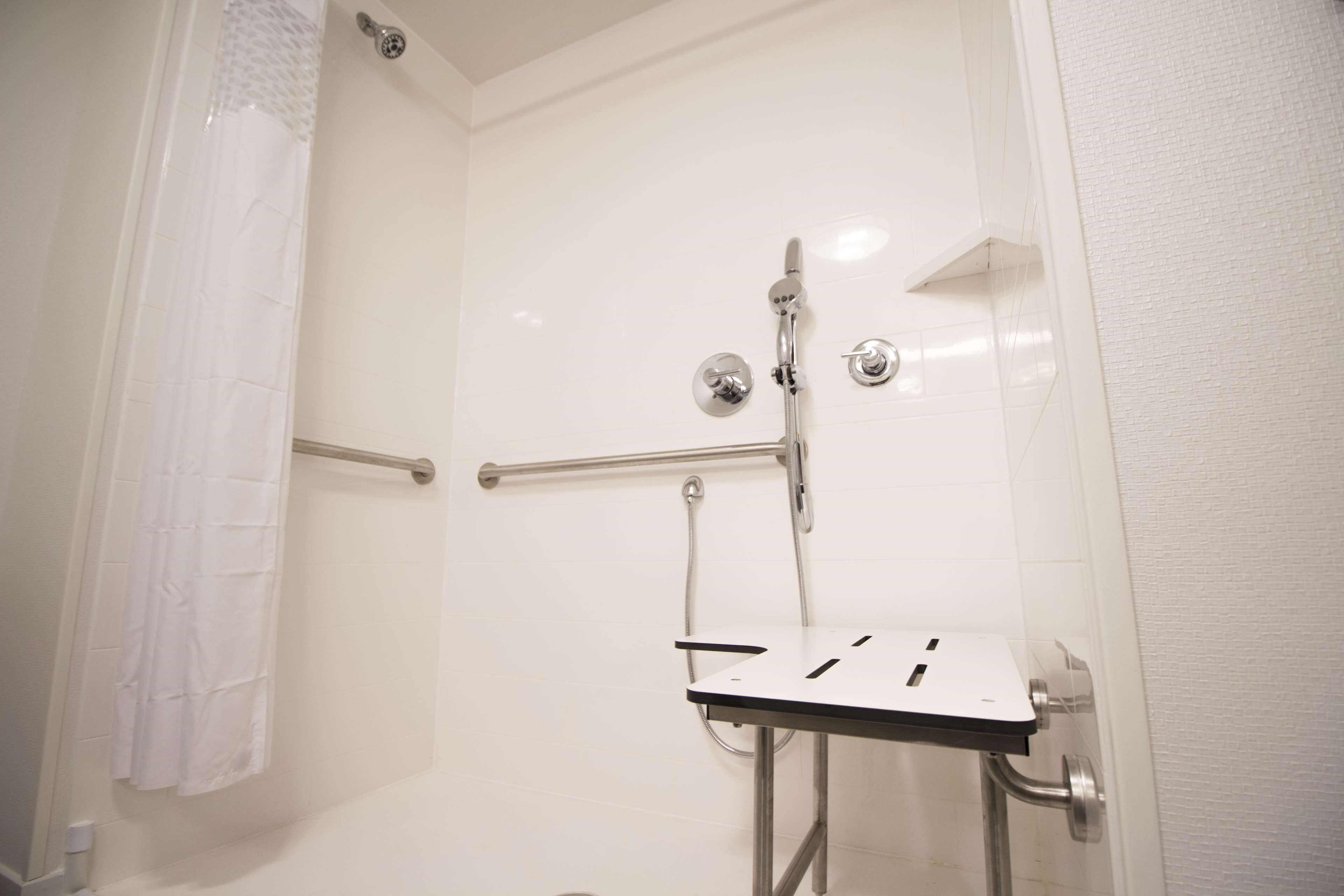 Un baño moderno con cabina de ducha de vidrio, un lavamanos blanco y encimera negra, y un perchero para toallas.