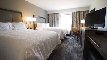 A hotel room with two beds, a desk with a TV, and a window with curtains.