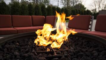 A fire pit with burning logs surrounded by red cushioned seating.