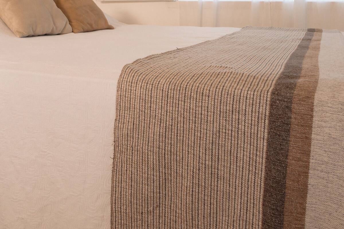 A bedroom with a large bed, a window with sheer curtains, and a plain wall.
