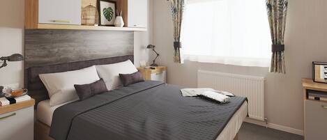 A bedroom with a bed, bedside tables, a nightstand, a window with curtains, and a shelf with decorative items.
