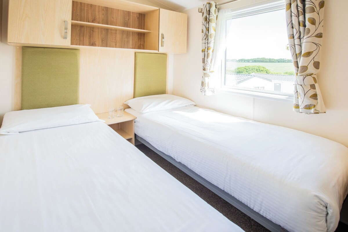 A single room with two beds, a wooden cabinet, a window with curtains, and a view of greenery outside.
