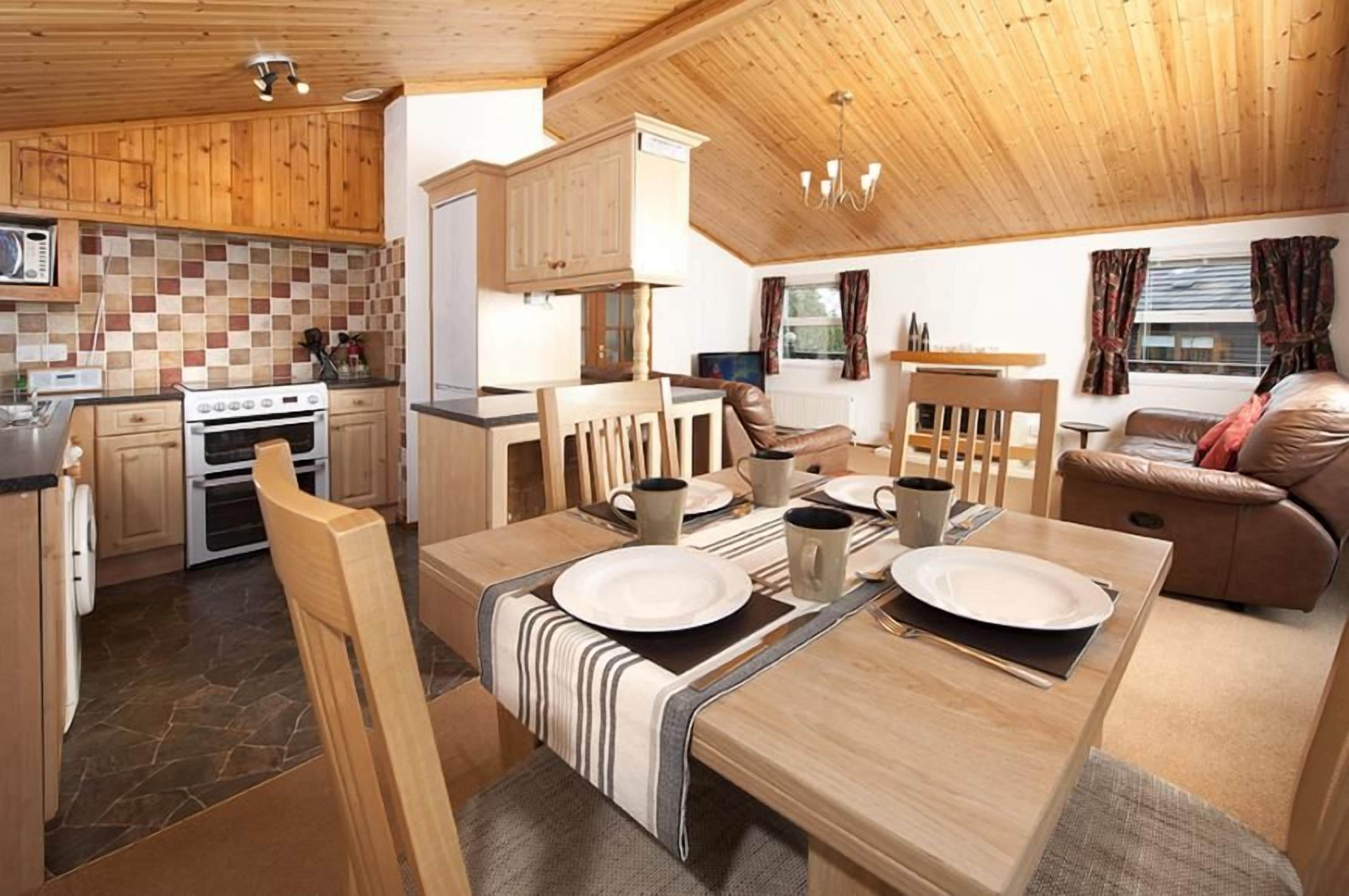 A cozy kitchen with wooden cabinets, a dining table set for two, and a living area with a sofa and a television.