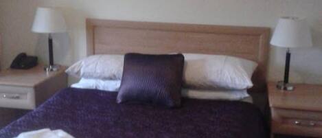 A hotel room with a large bed, two pillows, two bedside tables with lamps, and artwork on the walls.