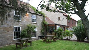 A stone building with a patio area featuring wooden tables and benches. - Cottage Lea's Country Hotel & Restaurant (Pickering)
