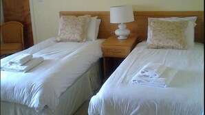A hotel room with two single beds, a nightstand with a lamp, and a floral painting on the wall. - Cottage Lea's Country Hotel & Restaurant (Pickering)
