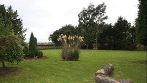 A grassy area with a small bush of tall, light-colored flowers, a few trees, and a large log on the ground. - Cottage Lea's Country Hotel & Restaurant (Pickering)
