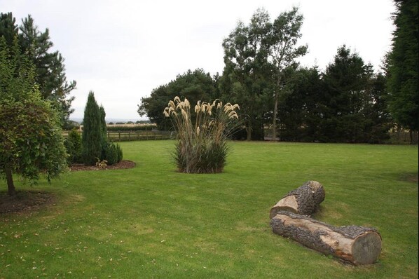 A grassy area with a small bush of tall, light-colored flowers, a few trees, and a large log on the ground. - Cottage Lea's Country Hotel & Restaurant (Pickering)