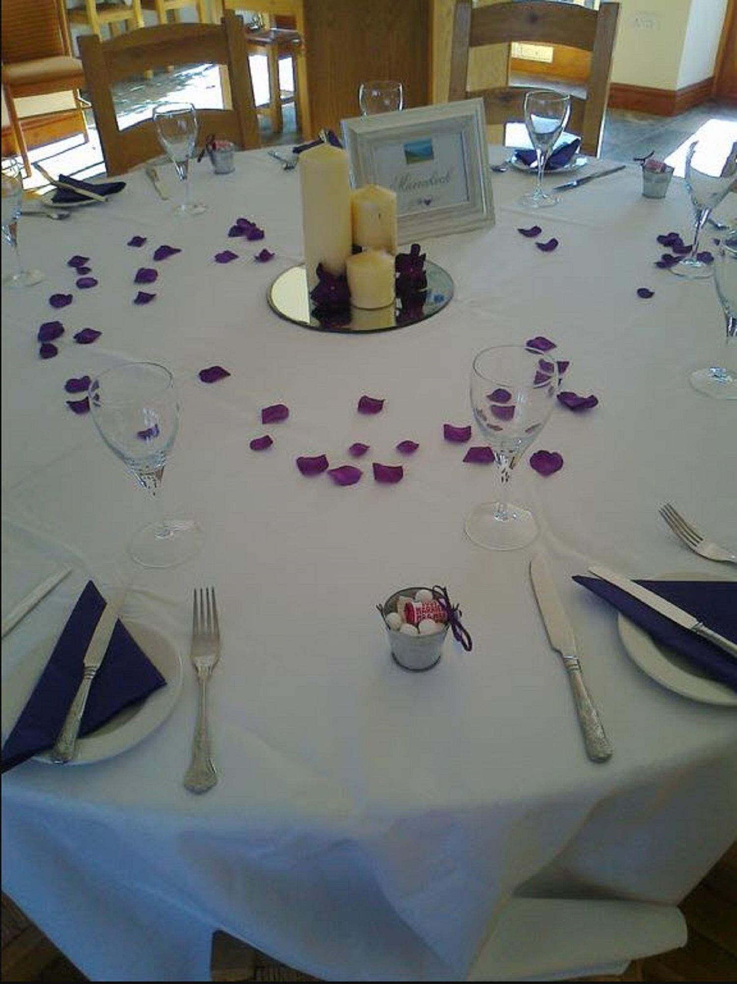 A table set for a meal with a white tablecloth, candles, and purple flower petals.