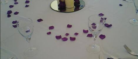 A table set for a meal with a white tablecloth, candles, and purple flower petals.