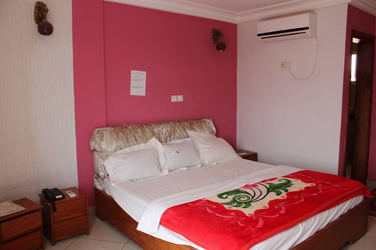 A bedroom with a bed, a nightstand, an air conditioning unit, and a door.