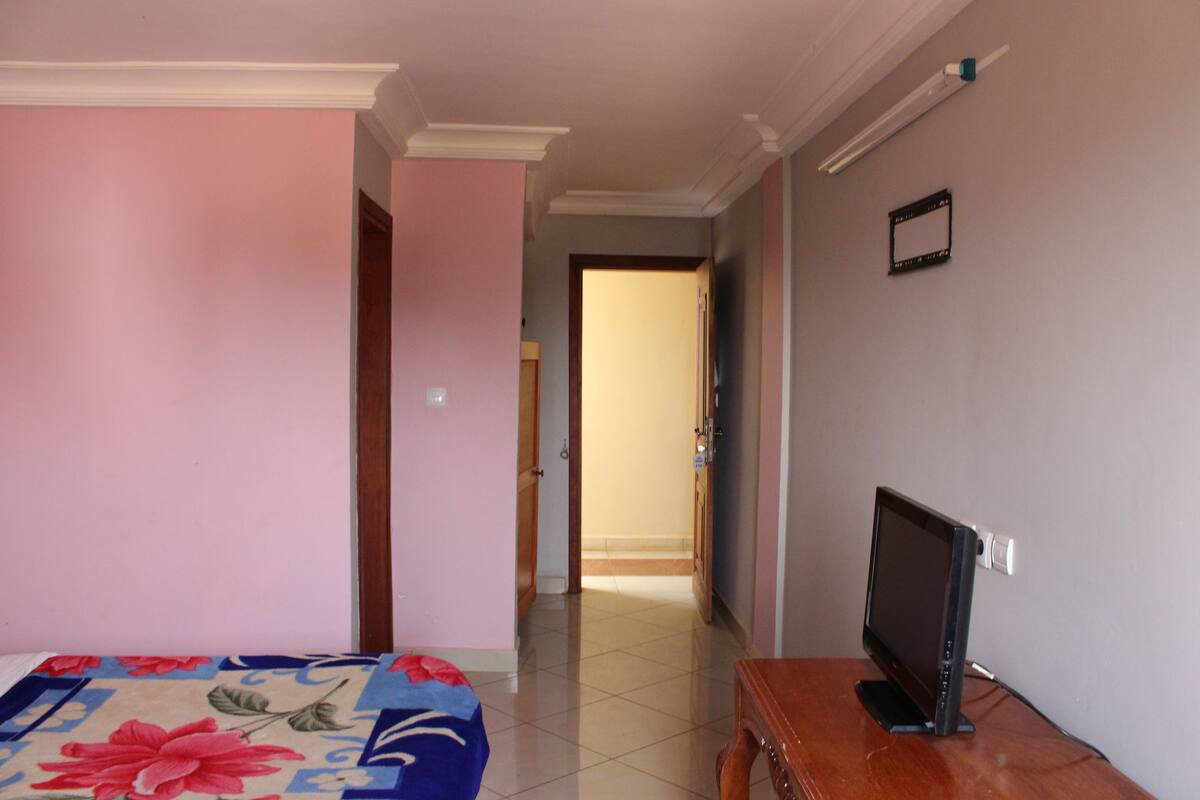 A hotel room with a bed, a TV on a wooden table, and a door leading to another room.
