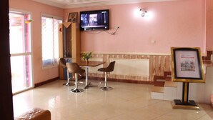 Un área de recepción con un televisor montado en la pared, un cuadro enmarcado y una pequeña mesa con sillas.