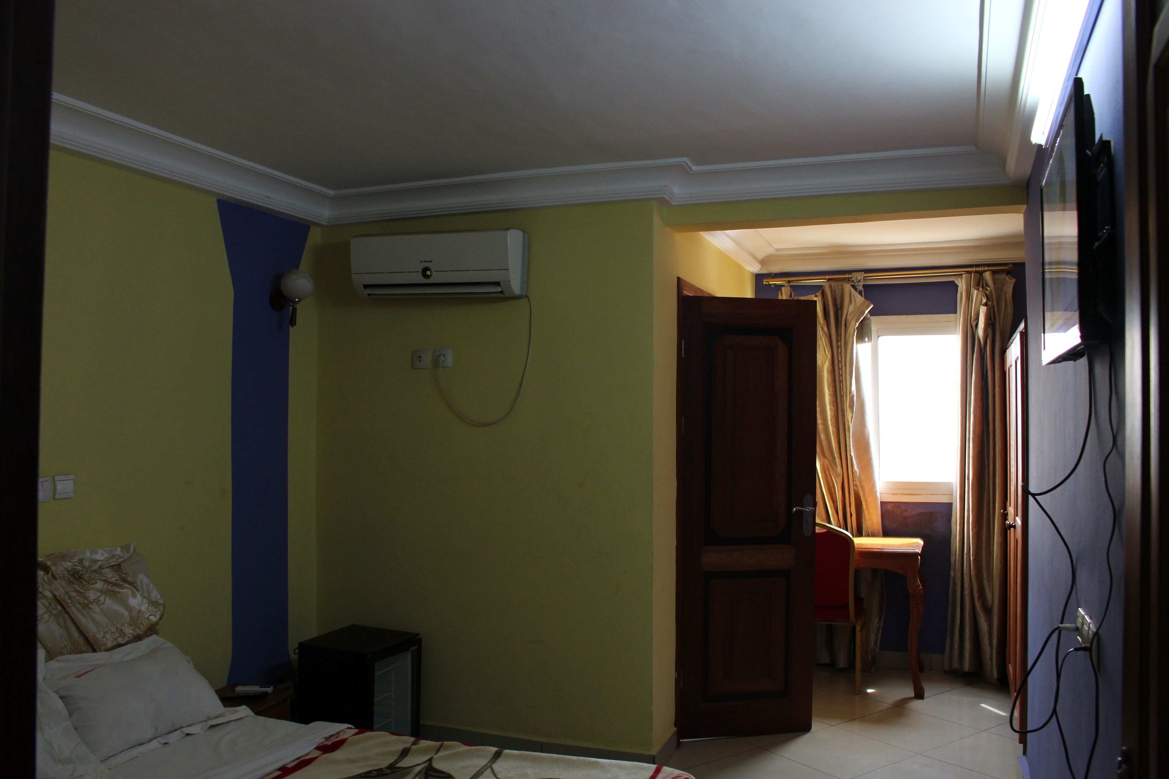 A bedroom with a bed, an air conditioner, a desk, and a chair.