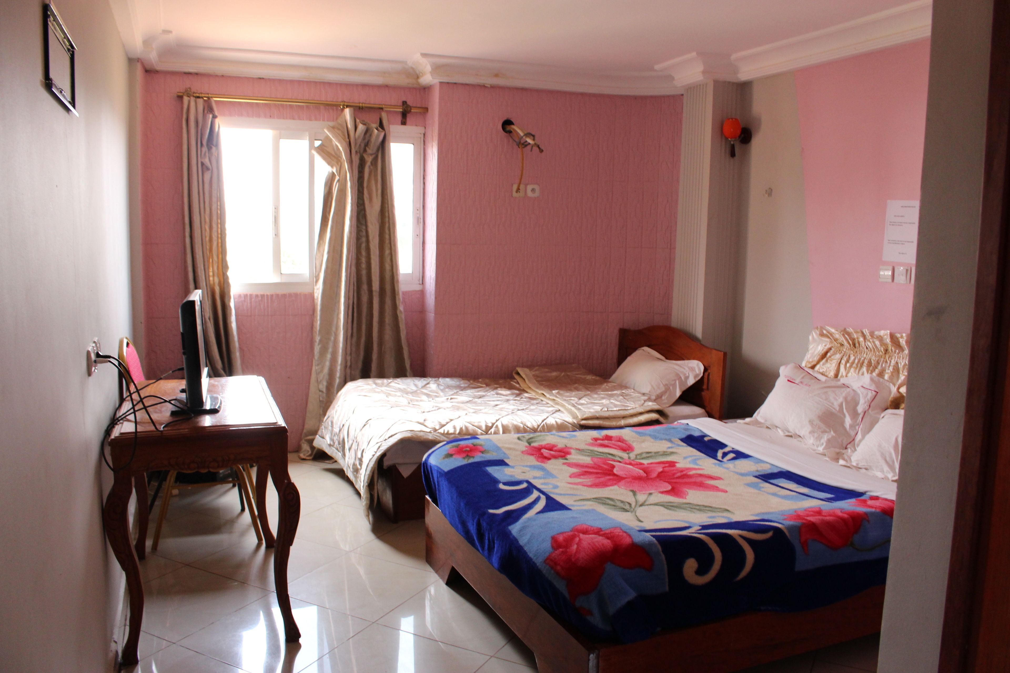 A bedroom with a bed, a desk, and a window with curtains.