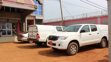 A hotel with a sign reading "MBATKAMHOTEL" and two white Toyota pickup trucks parked in front.