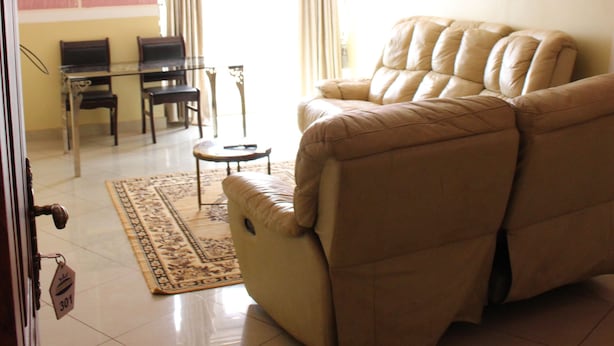 Una sala de estar con un sofá beige, una mesa de centro de vidrio y un comedor con sillas y una mesa.