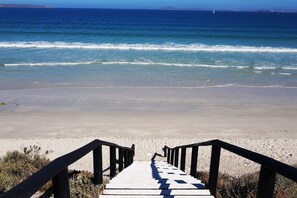 Een houten trap die naar een strand leidt met helderblauw water en land in de verte.