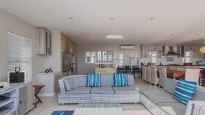 A modern living room with a sectional sofa, a dining area with wicker furniture, and a kitchen with built-in cabinets. - Seasons of Serenity, Langebaan 8-sleeper (Langebaan)