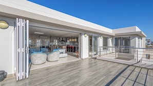 A modern, open-plan living area with a kitchen, dining space, and a balcony with outdoor seating. - Seasons of Serenity, Langebaan 8-sleeper (Langebaan)
