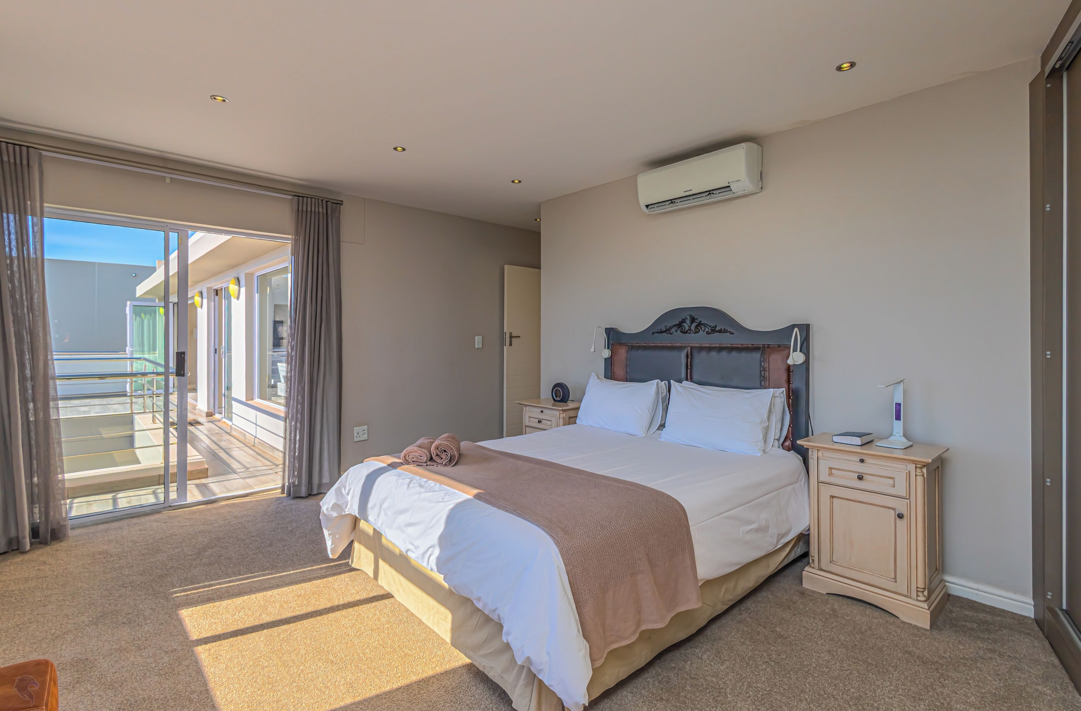 Ein Hotelzimmer mit einem großen Bett, einem Nachttisch, einer Klimaanlage und einer Glastür, die auf einen Balkon führt.