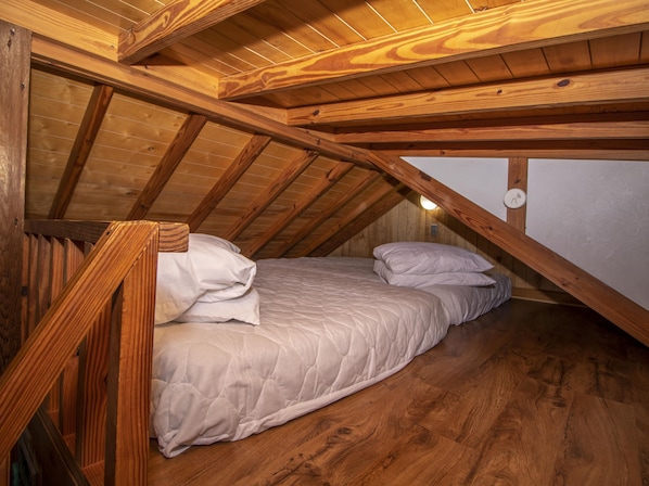 Une petite chambre mansardée, chaleureuse et accueillante, avec un plafond en bois et un toit en pente, comprenant un lit simple avec une couette et des oreillers blancs.