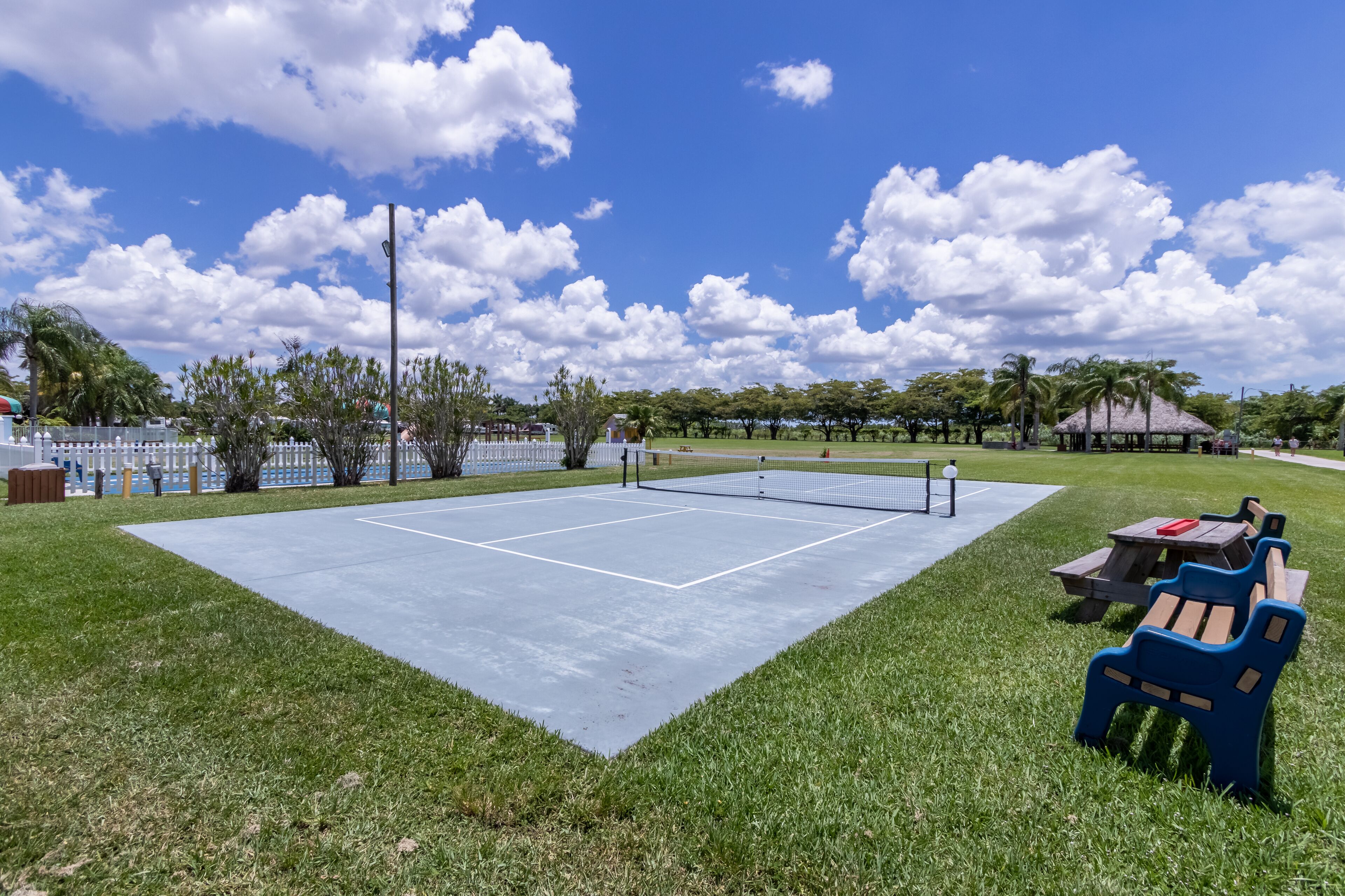 An outdoor tennis court with a net, surrounded by grass and trees.