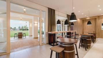 Zona de bar moderna con barriles de madera como taburetes, grandes lámparas colgantes y un puerta de cristal que da a un patio al aire libre.