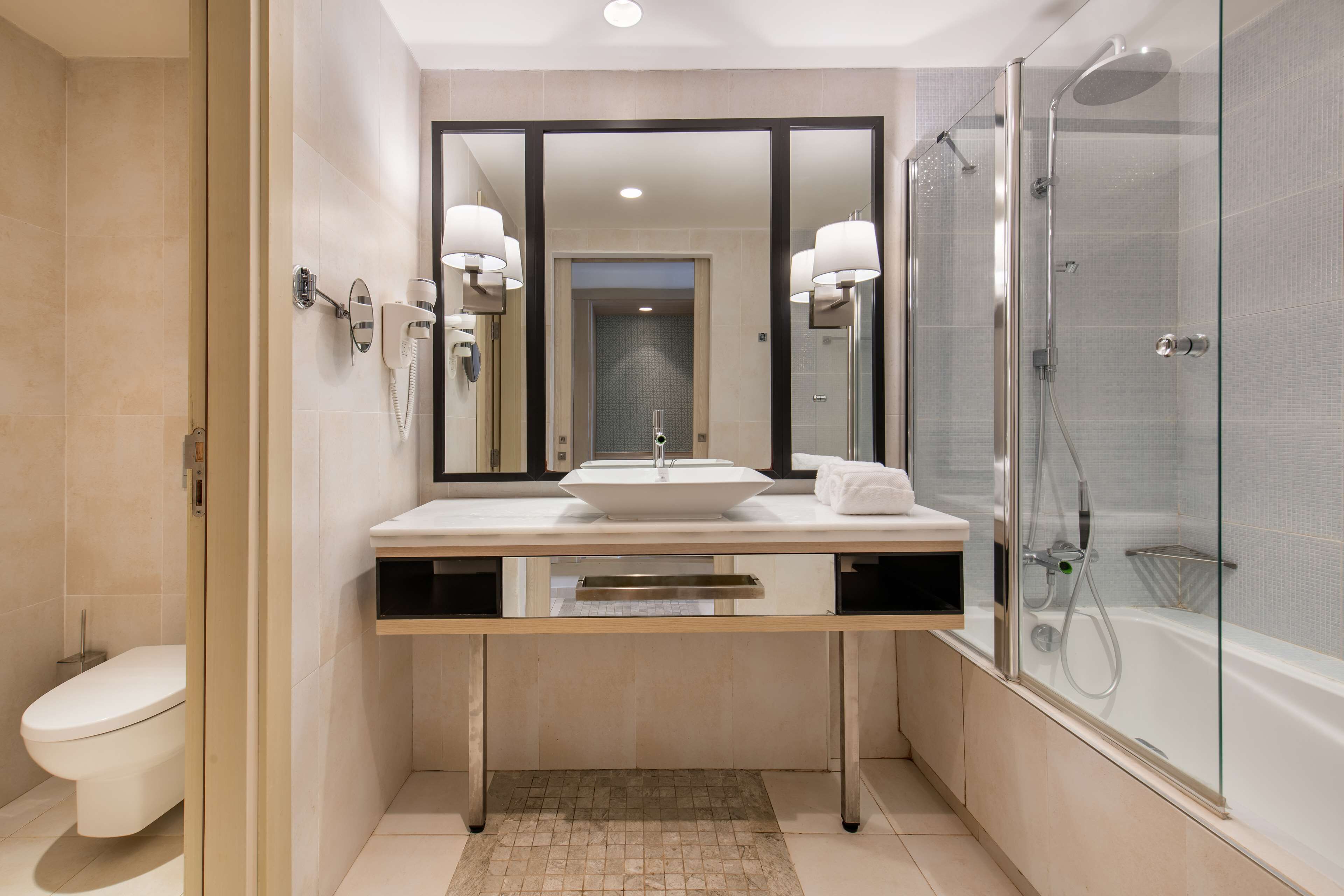 A modern bathroom with a large mirror, a sink, a toilet, and a glass-enclosed shower.