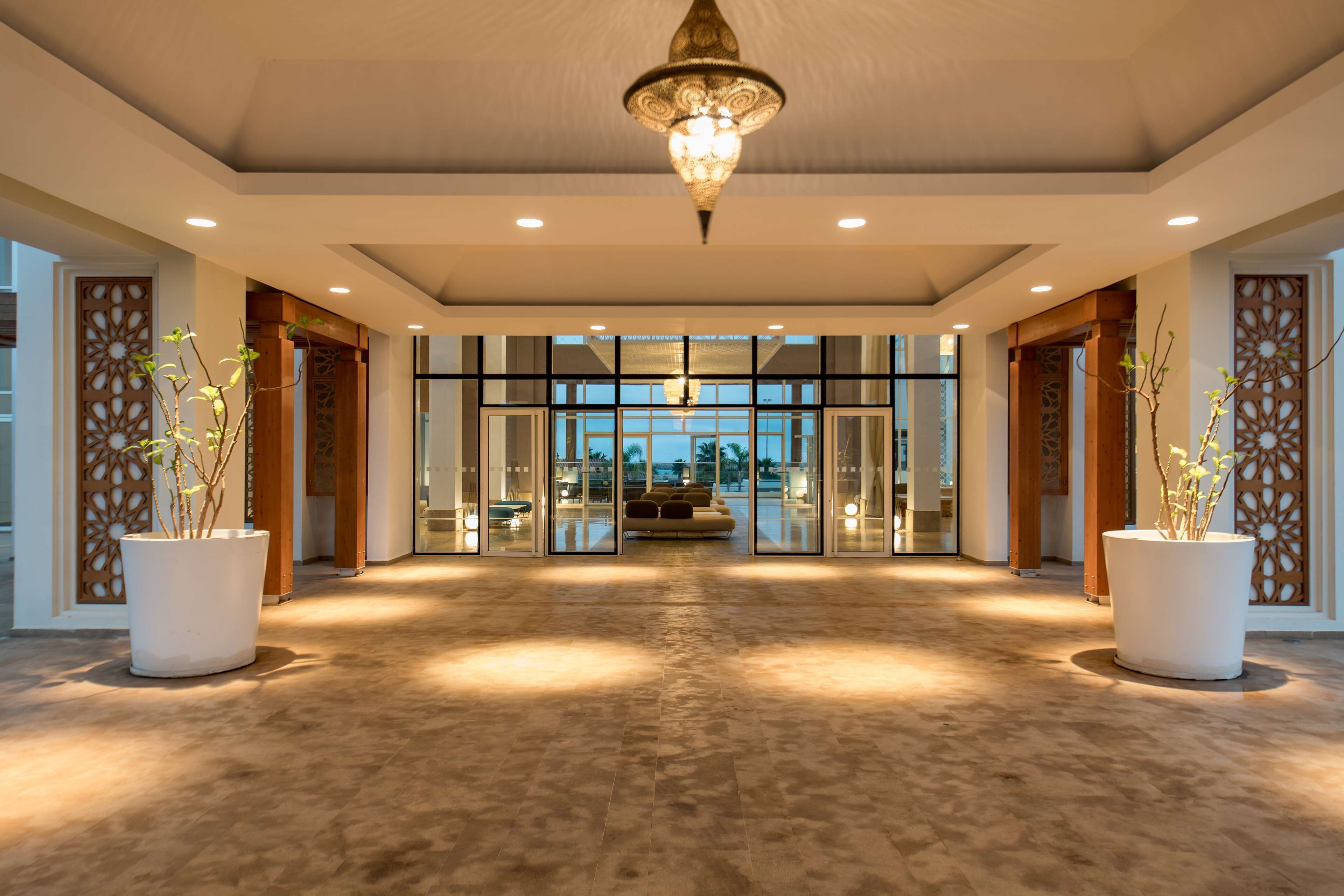 A spacious lobby with a high ceiling, large potted plants, and a central seating area.