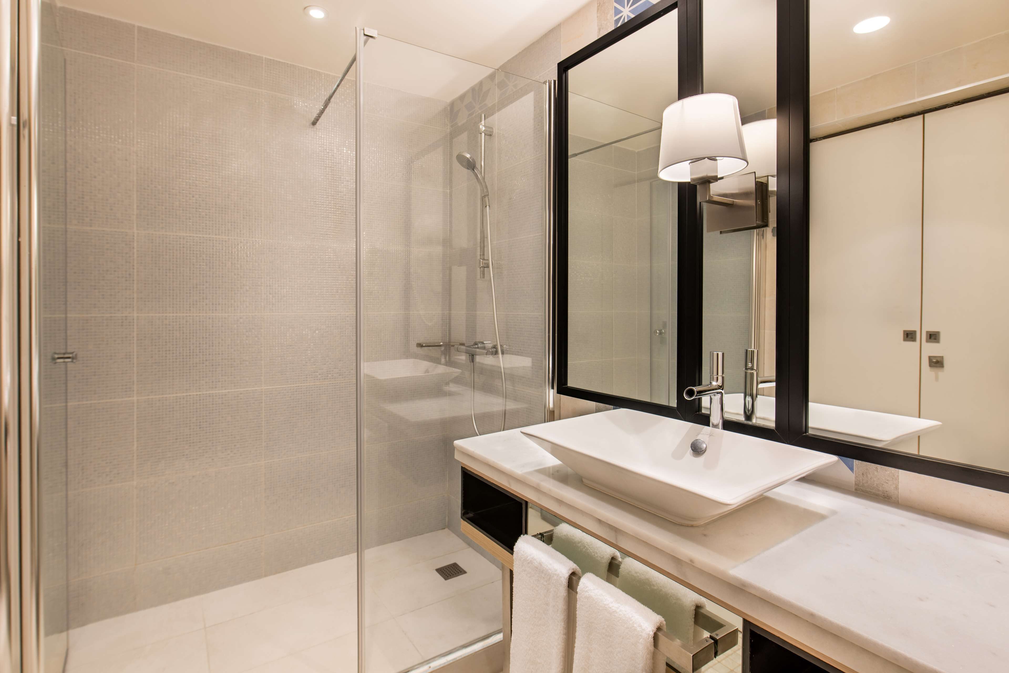 Un baño moderno con ducha envuelta en vidrio, un espejo grande y un lavamanos blanco.