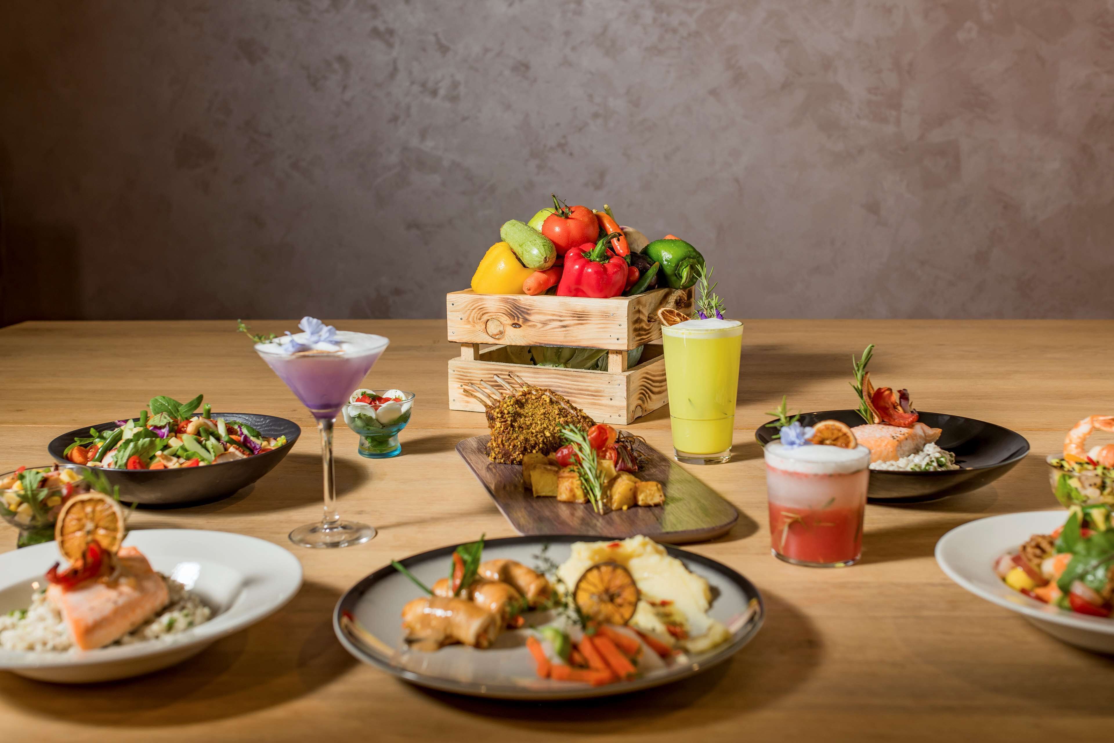 Une table en bois sur laquelle on trouve différents plats, notamment du saumon, des légumes et un panier de fruits.
