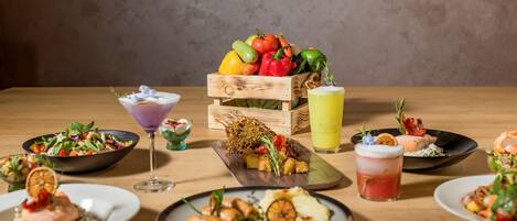 Une table en bois sur laquelle on trouve différents plats, notamment du saumon, des légumes et un panier de fruits.