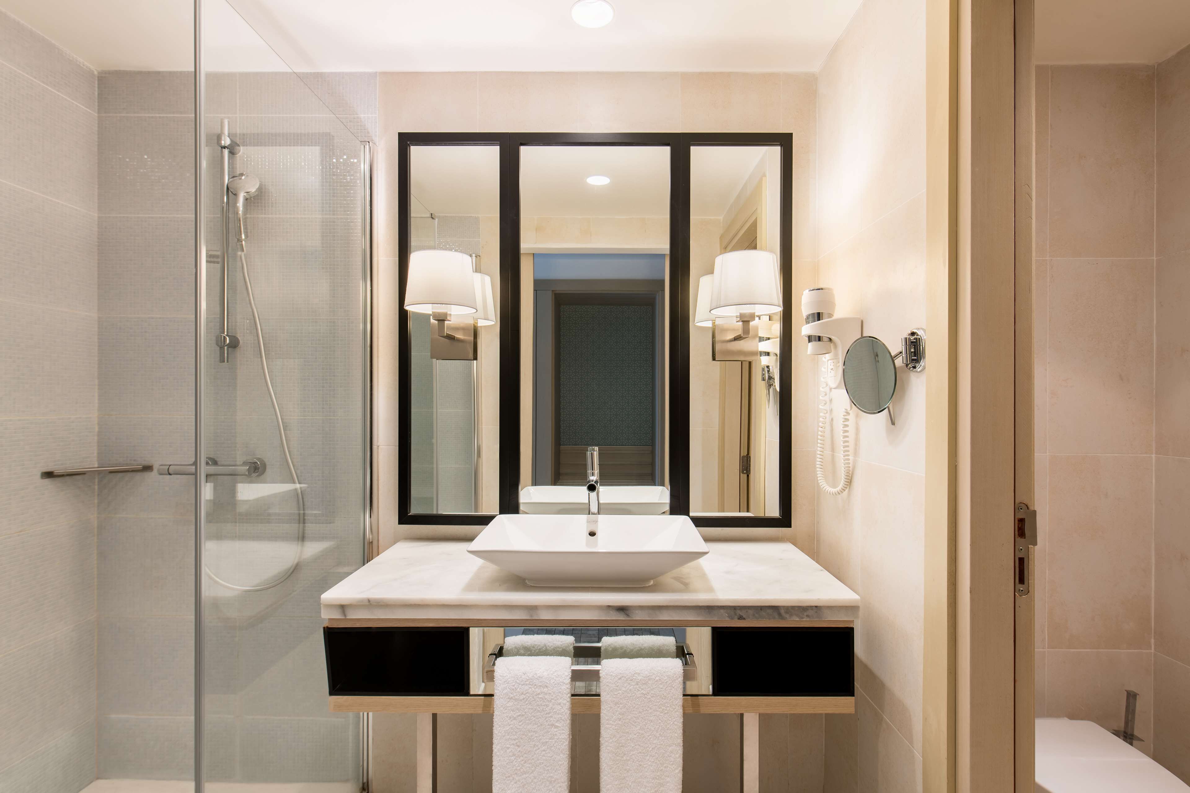 A modern bathroom with a glass-enclosed shower, a large mirror, a white sink, and a towel rack.