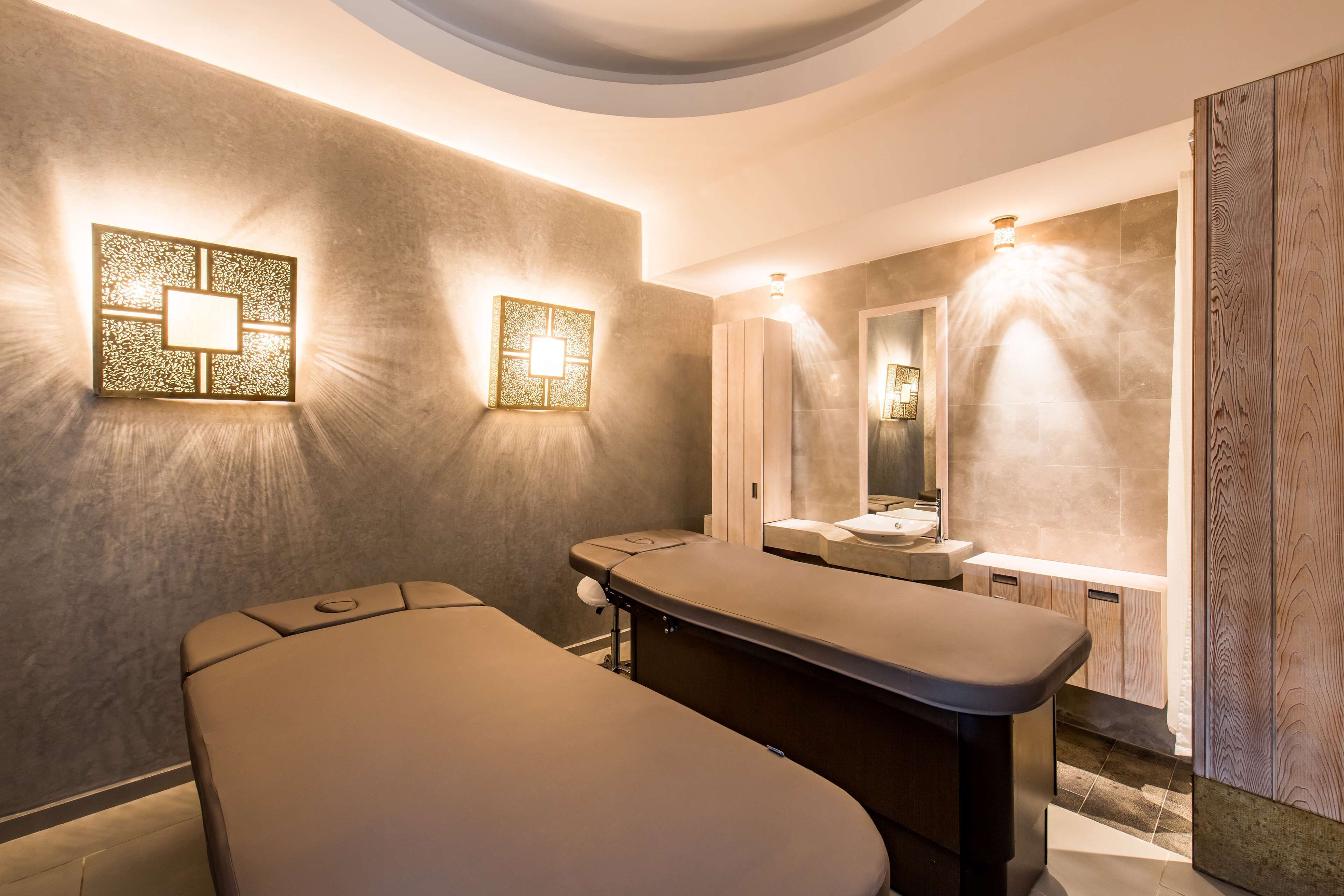 A modern spa room with a massage table, a large mirror, and wall-mounted lighting fixtures.