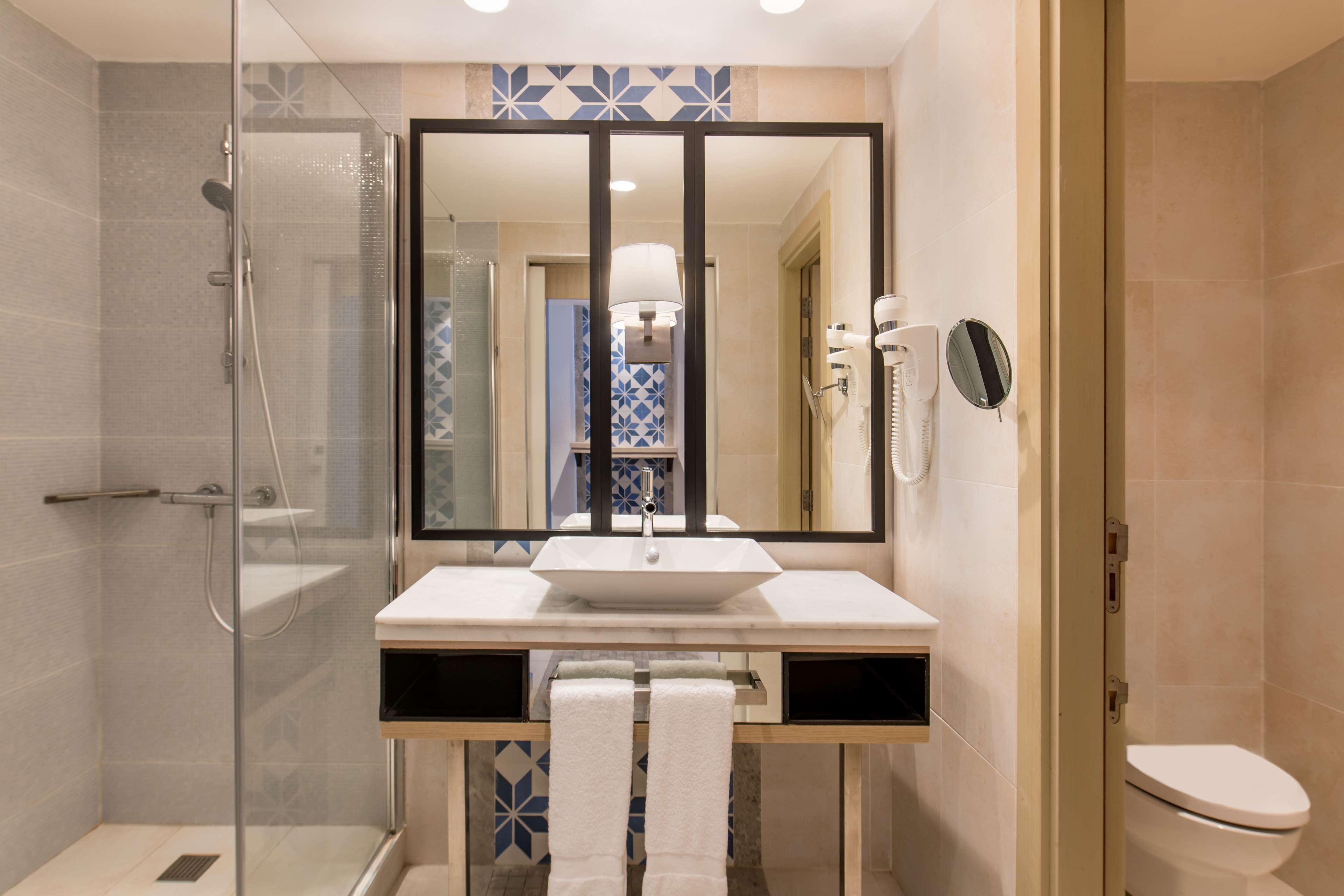 Un baño moderno con cabina de ducha de vidrio, un espejo grande, un lavabo blanco y un inodoro.