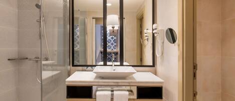 Un baño moderno con cabina de ducha de vidrio, un espejo grande, un lavabo blanco y un inodoro.