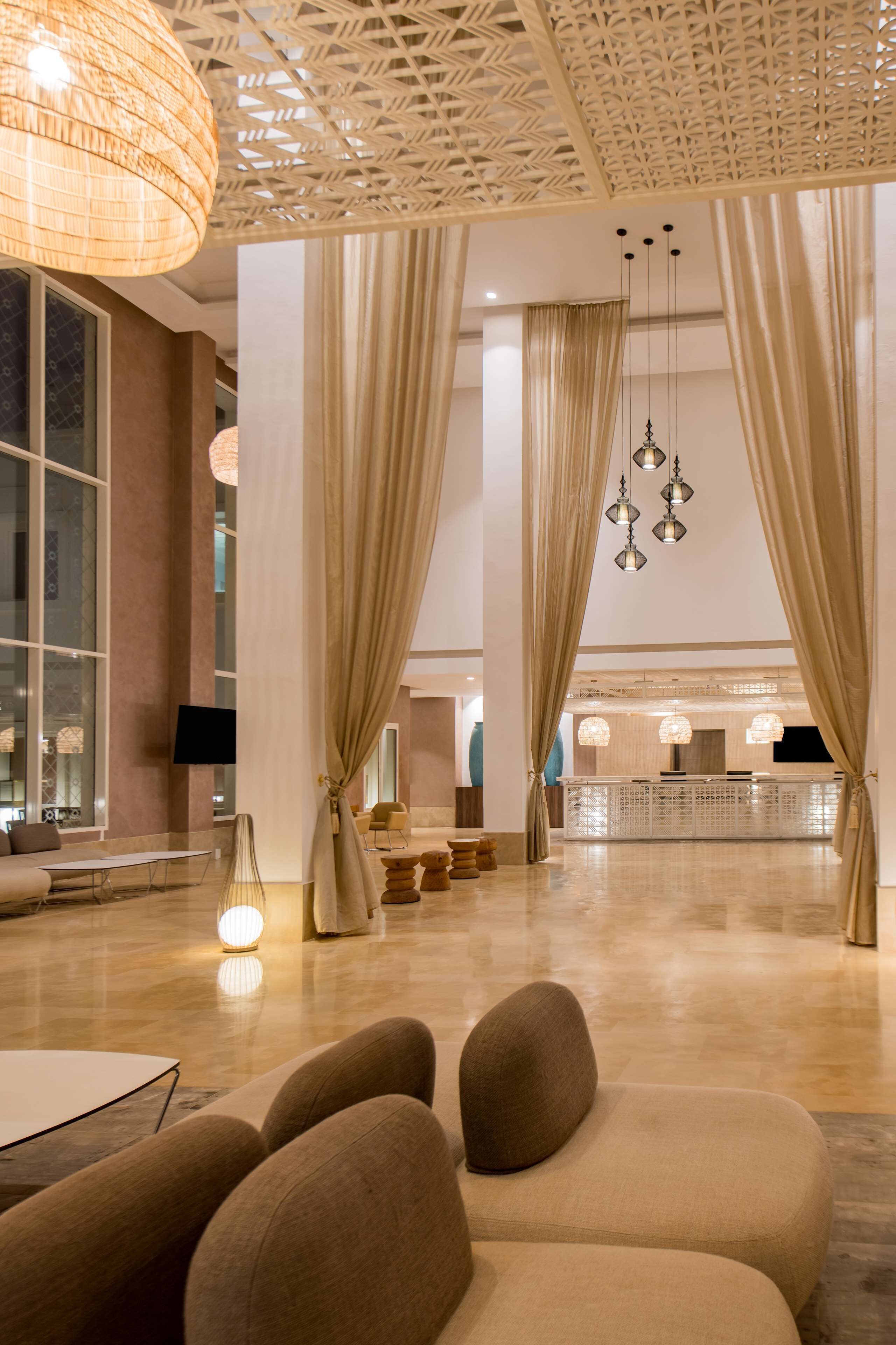 A spacious lobby with a modern design, featuring a reception desk, comfortable seating, and decorative lighting.
