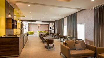 A modern hotel lobby with a long reception desk, multiple seating areas, and a large window with curtains.