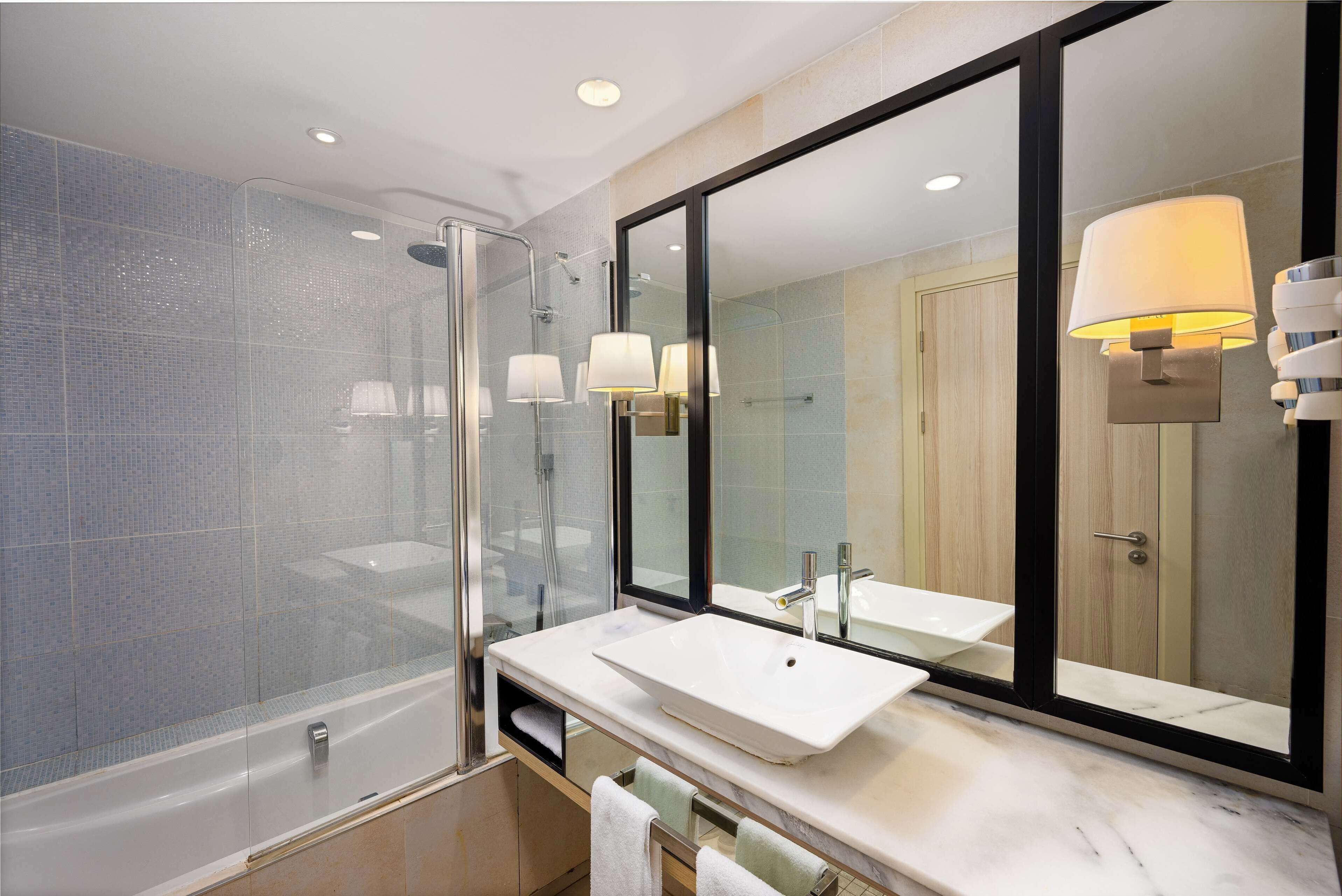 A modern bathroom with a glass-enclosed shower, a large mirror, and a marble countertop.