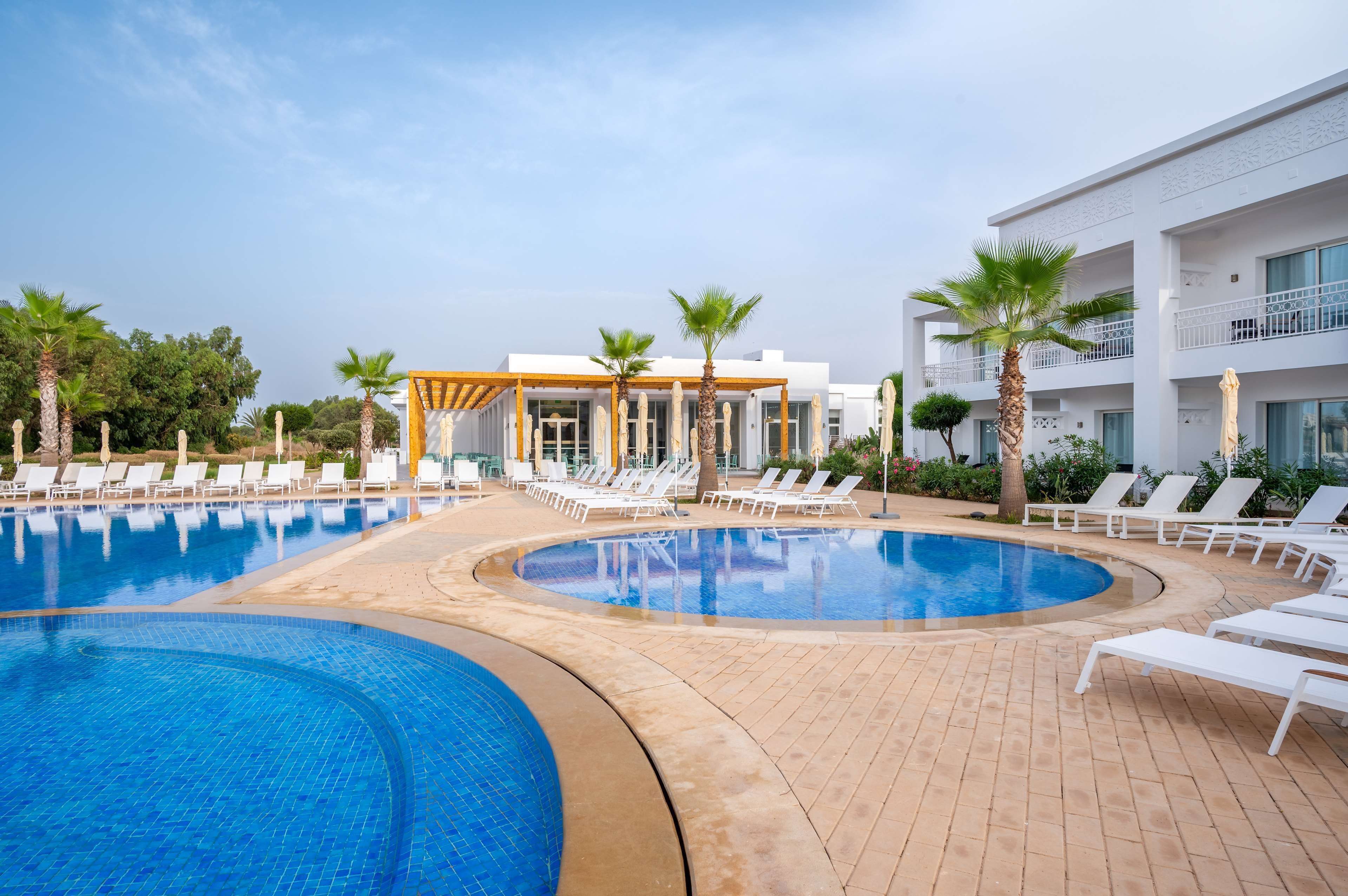 A hotel pool area with two separate pools, lounge chairs, and palm trees.