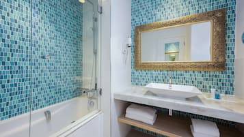Une salle de bain dotée d’une douche à parois de verre, d’un lavabo blanc avec un plan de toilette en marbre et d’un miroir décoratif orné d’un cadre doré.